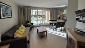Ein modernes Wohnzimmer mit Sofa, Couchtisch und Fernseher. Es gibt einen Essbereich mit Tisch und Stühlen. Das Zimmer verfügt über große Fenster und einen Ausblick nach draußen.