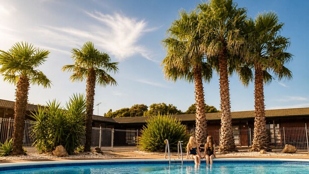 A swimming pool surrounded by palm trees and a building with a tiled roof. - Compact, Cosy Studio (Gisborne)