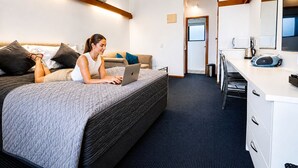 A modern hotel room with a bed, a desk, a microwave, and a large mirror. - Compact, Cosy Studio (Gisborne)
