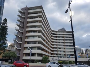 A multi-story hotel with a curved facade, balconies on each floor, and a sign indicating the name 'The Sands' with the number 40.