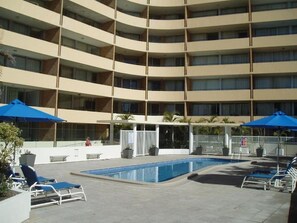Ett hotell med flera våningar, en swimmingpool och solstolar.