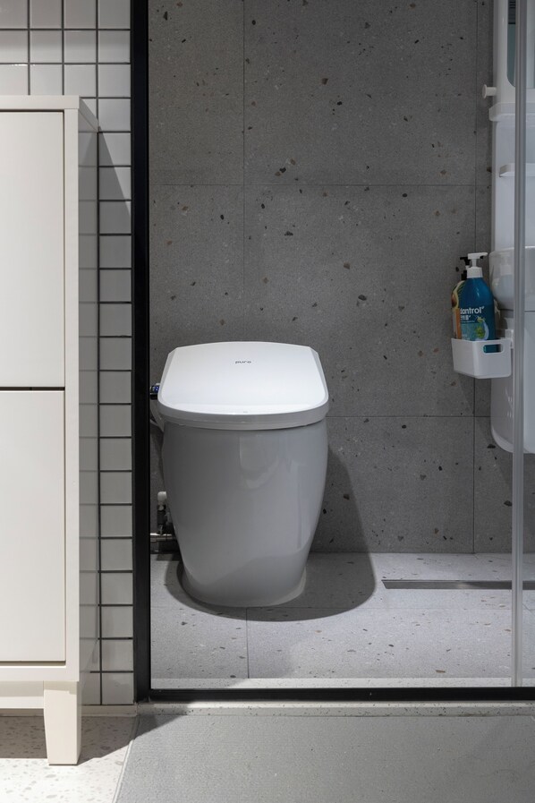 Un baño moderno con inodoro blanco, pared con azulejos y mueble blanco.