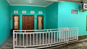 A turquoise house with a white railing, two wooden doors, and a small porch. - Bronk House (Yogyakarta)