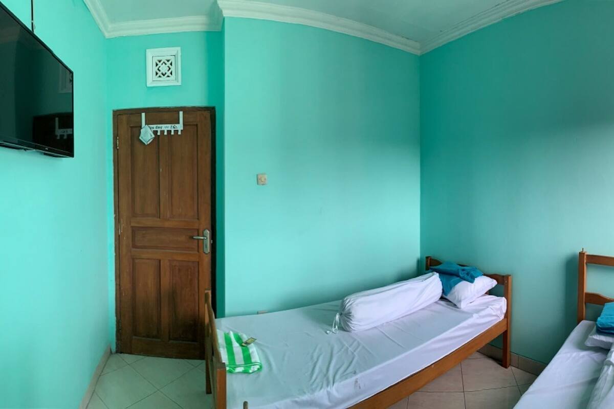 A room with teal walls, a wooden door, a bed with white bedding, a small wooden table, and a TV mounted on the wall.
