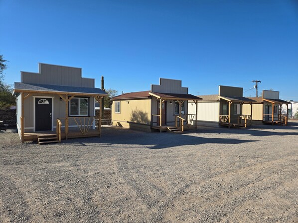 A row of small, single-story buildings with wooden porches and steps leading to the door. - Westworld Cabins (Quartzsite)