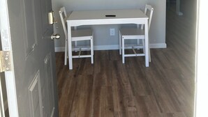 Un coin repas avec une table et des chaises blanches, un ventilateur de plafond et un tableau représentant des chevaux accroché au mur.