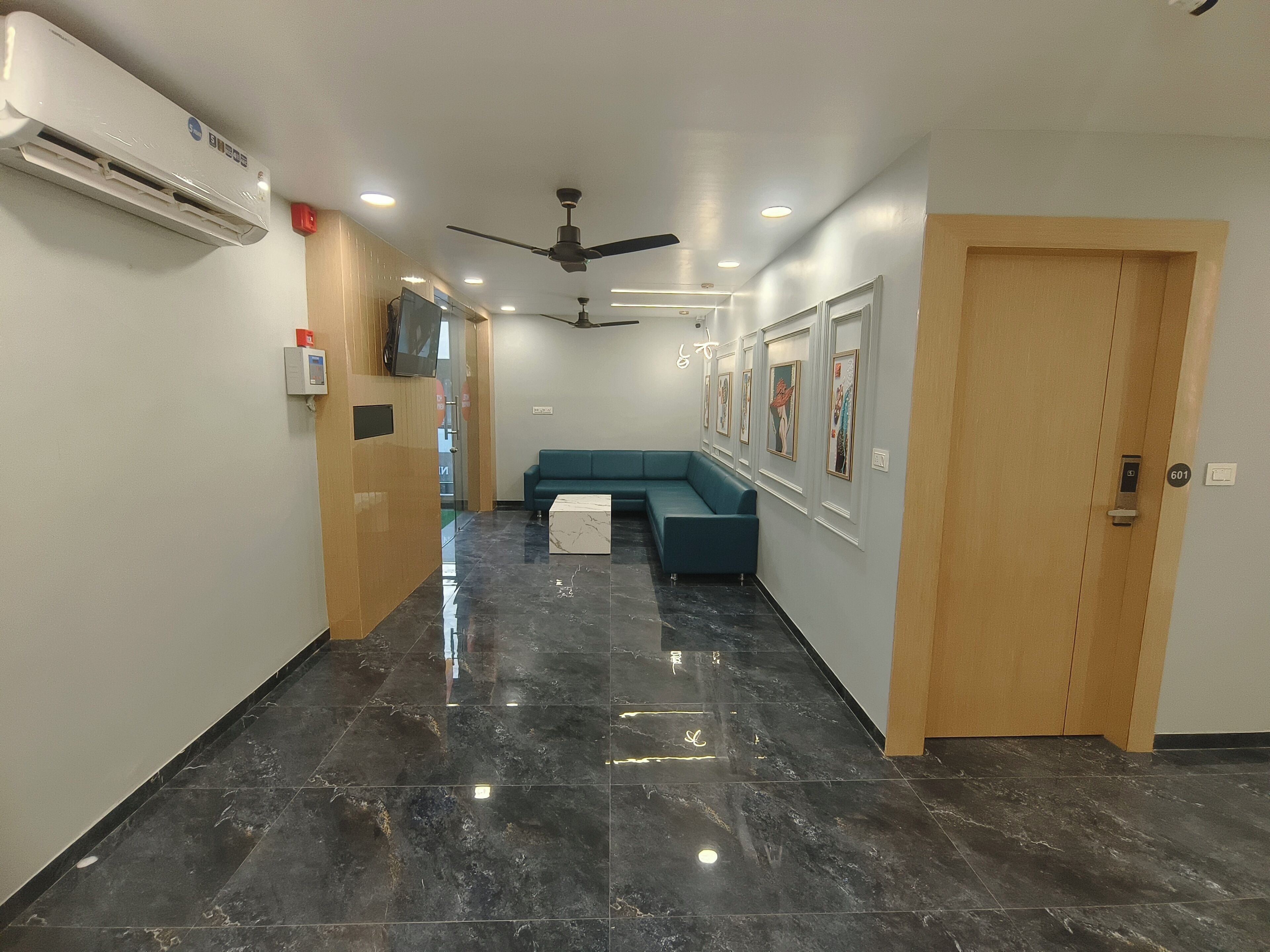 A modern hallway with a marble floor, a blue sofa, and a ceiling fan.