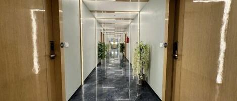 A modern hotel hallway with marble flooring, wooden doors, and potted plants.
