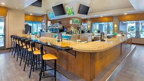 Un área de bar moderna con una barra larga, varios taburetes y una pantalla de televisión montada en el techo.
