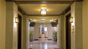 Un pasillo de hotel con piso pulido, lámparas simétricas y plantas en macetas.