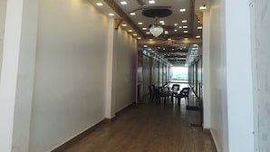 A hallway with a wooden floor, ceiling lights, and a chandelier. - Hotel King Palace (Kilvelur)