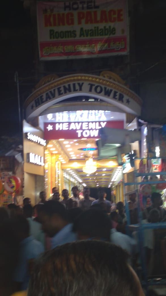 A crowded entrance to a hotel named "Heavenly Tower" with a sign indicating "Rooms Available".