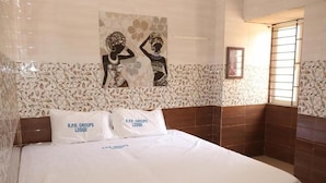 A hotel room with a bed, two pillows with 'R.P.R. GROUPS LODGE' text, a decorative wall with a floral pattern, and a window with bars. - Hotel King Palace (Kilvelur)