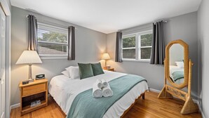 Ein Schlafzimmer mit einem Bett, zwei Nachttischen, einem Spiegel und einem Fenster mit Vorhängen.