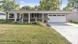 Ein eingeschossiges Haus mit Veranda, Garage und gepflegtem Rasen.