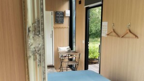 Ein Zimmer mit einem Bett, einem kleinen Tisch mit Stuhl, einem Fenster und einer Tür, die nach draußen führt.
