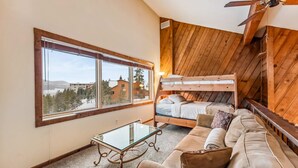 A room with a bunk bed, a glass-top table, a sofa, and a large window offering a view of buildings and trees. - Dillon Retreat with Lake Views and Private Hot Tub (Dillon)