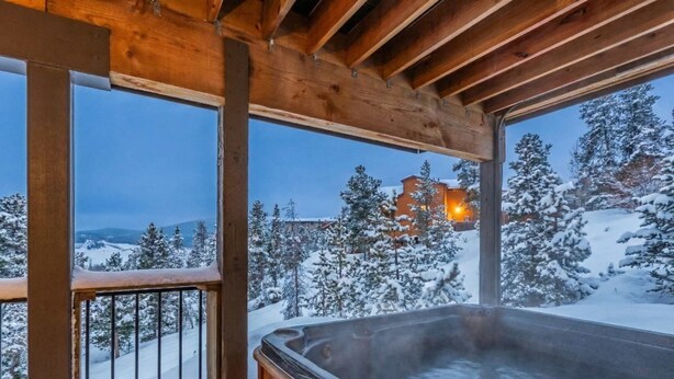 A wooden deck with a hot tub overlooking a snowy landscape and a building in the distance. - Dillon Retreat with Lake Views and Private Hot Tub (Dillon)