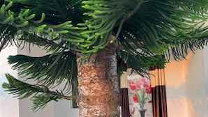 A tree with a textured trunk, a tiled floor with a geometric pattern, and a wall with a floral painting and curtains. - Deers Eco Home Resort (Daringbadi)