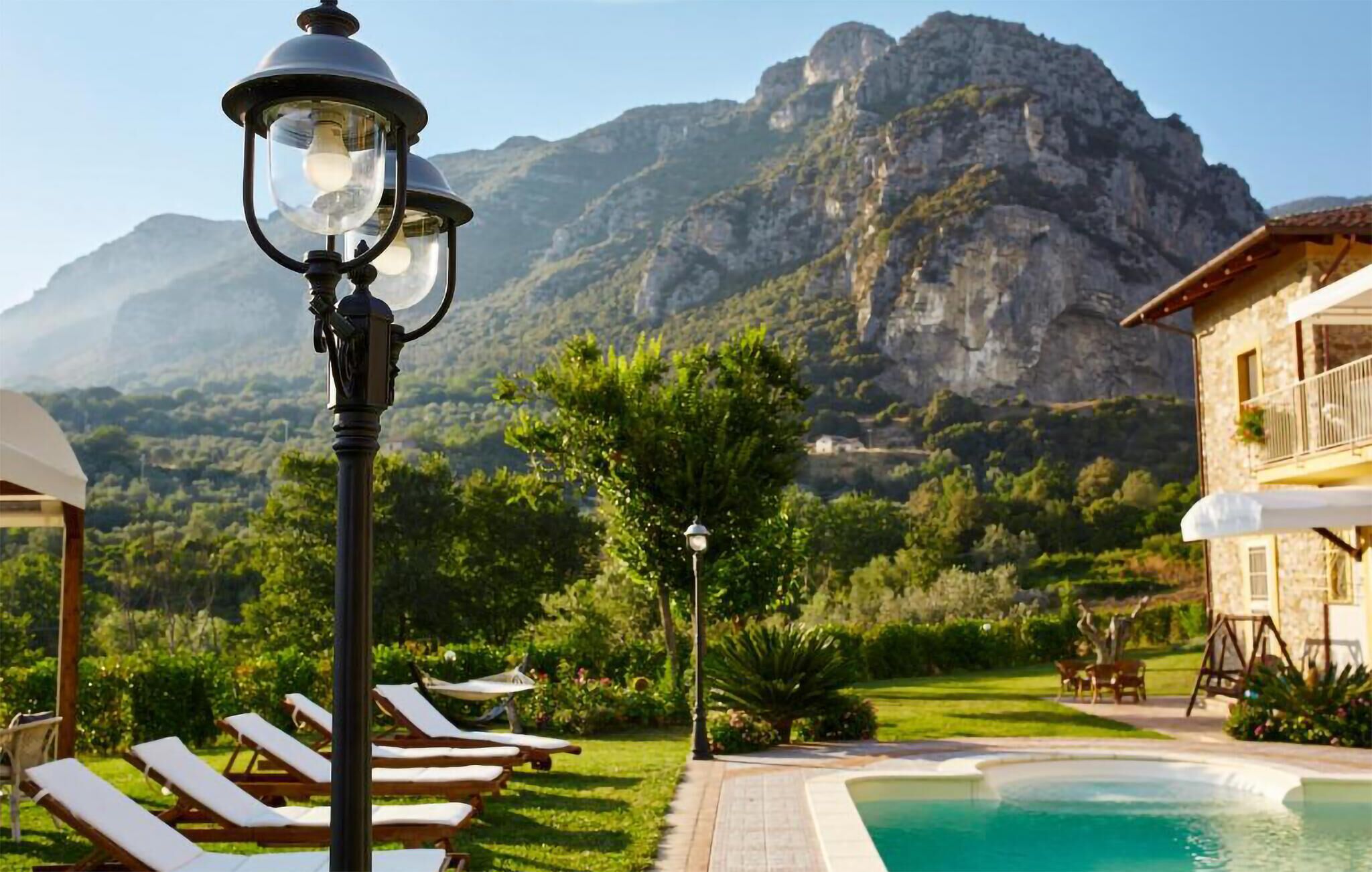A poolside area with lounge chairs, a lamp post, and a mountain backdrop.