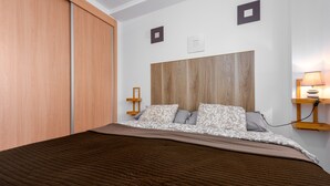 Un dormitorio con cama, cabecera de madera, mesitas de noche y una mesita auxiliar.