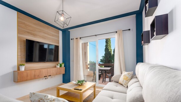 Una sala moderna con televisor de pantalla plana, sofá, mesa de centro y vista a un patio exterior a través de un ventanal.