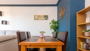 Un comedor con una mesa y sillas de madera, un letrero que dice 'WELCOME', un reloj de pared decorativo y una estantería con libros y una planta.