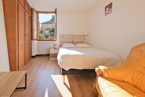 A bedroom with a bed, a wooden wardrobe, a nightstand, a lamp, a window with a view, and a sofa. - Le Pressoir – Authentic Holiday Home in the Heart of the Périgord Noir, Ideal for Families & Friends (Salignac-Eyvigues)