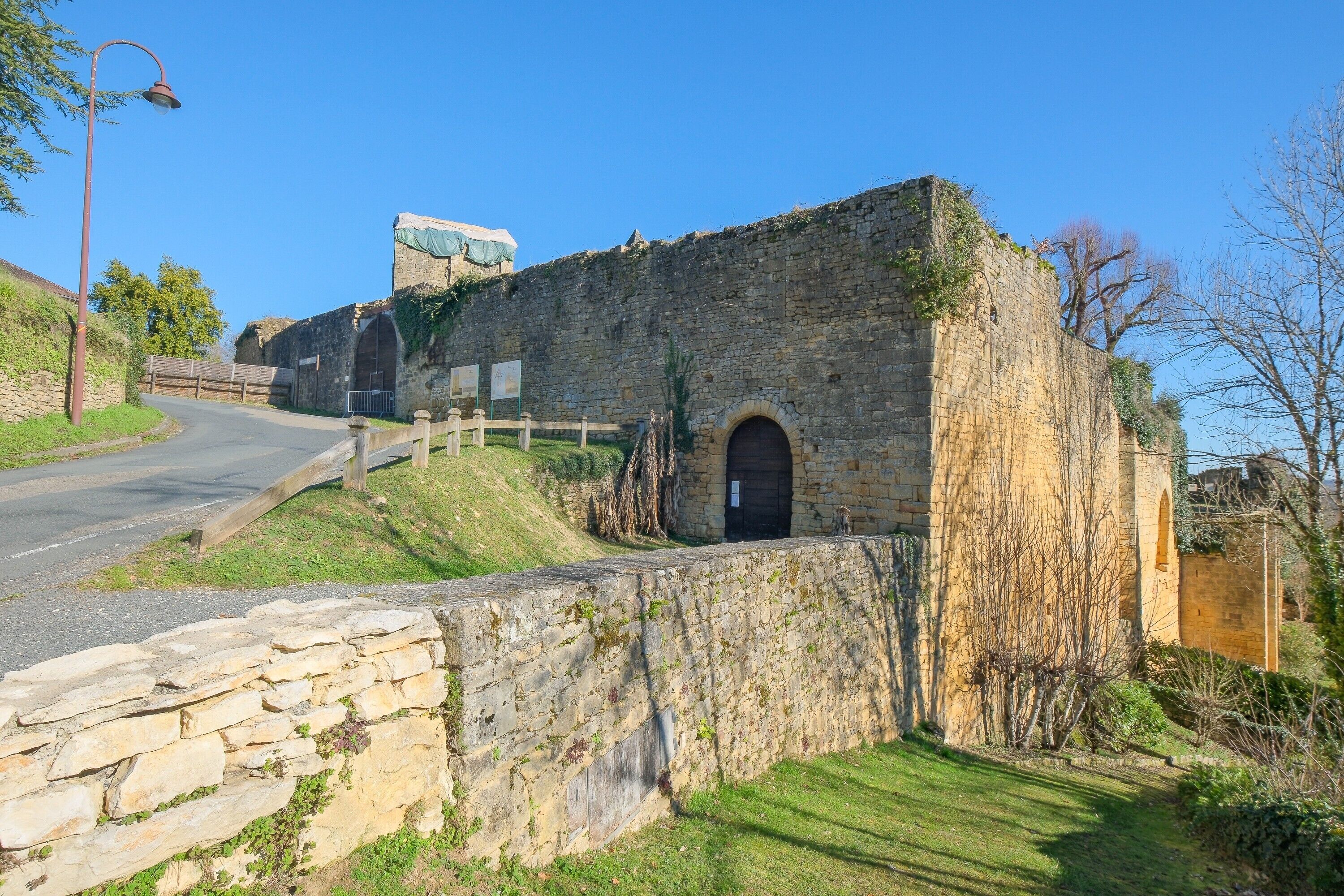 A stone building with a large arched doorway, a wooden fence, and a paved road.