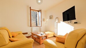 A living room with yellow furniture, a wooden coffee table, a flat-screen TV mounted on the wall, and a large window with a view. - Le Pressoir – Authentic Cottage in the Heart of Périgord Noir, Perfect for Families & Friends (Salignac-Eyvigues)