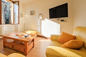 A living room with a wooden coffee table, a yellow sofa, a TV mounted on the wall, and a window with a view of a building. - Le Pressoir – Authentic Holiday Home in the Heart of the Périgord Noir, Ideal for Families & Friends (Salignac-Eyvigues)