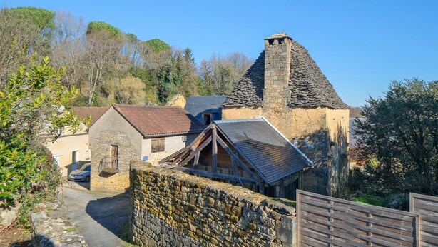 A stone building with a steep roof and a small tower, surrounded by trees and a stone wall. - Le Pressoir – Authentic Cottage in the Heart of Périgord Noir, Perfect for Families & Friends (Salignac-Eyvigues)
