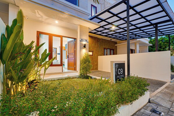 A modern villa with a covered outdoor area, a well-maintained garden, and a sign indicating the villa name and suite number.