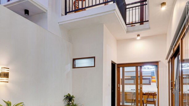 A modern pool area with a wooden deck, a glass-enclosed pool, and a balcony with a railing. - Villa Prinz near Nusa Dua Beach (Nusa Dua)