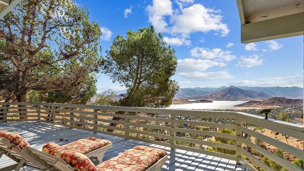 A balcony with wooden railings and cushioned seating, overlooking a scenic valley and mountains.