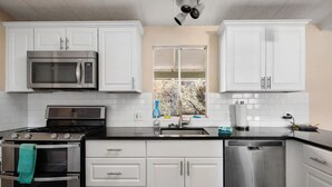 A modern kitchen with white cabinets, a stainless steel stove, a microwave, and a dishwasher.