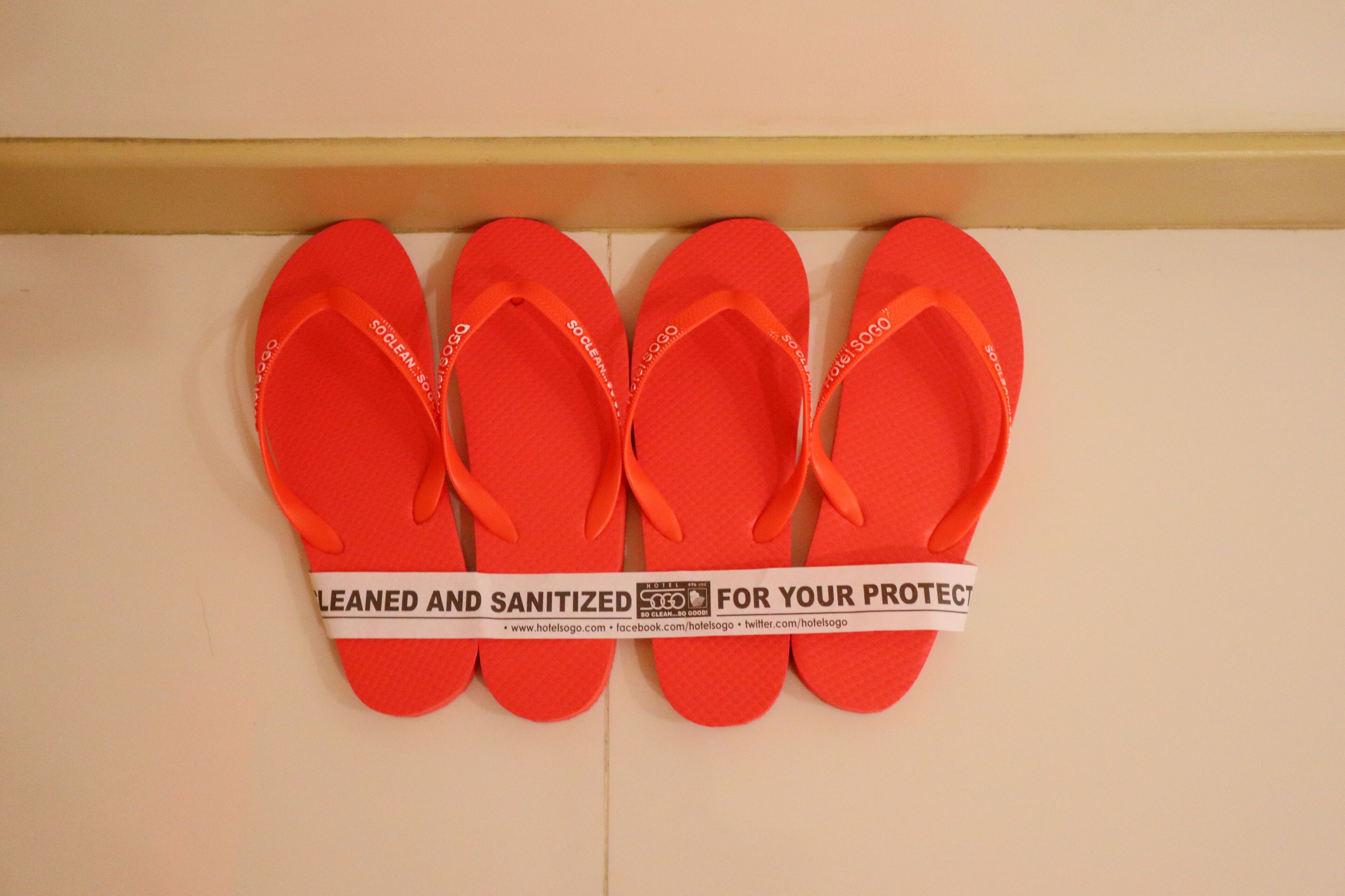 Quatre paires de tongs rouges sont accrochées à un mur, accompagnées d’une étiquette indiquant : « Nettoyées et désinfectées pour votre protection. »