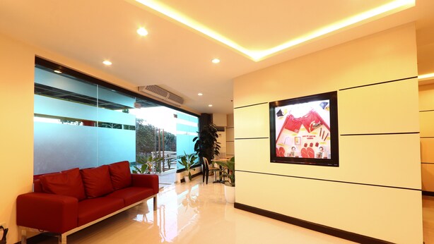 Un hall d’entrée moderne avec un canapé rouge, un grand écran de télévision et un mur de verre donnant sur l’extérieur.
