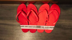 Une paire de tongs rouges, avec une étiquette indiquant qu’elles ont été désinfectées à des fins de protection.