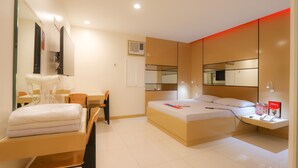 Une chambre d’hôtel moderne équipée d’un lit, d’une table de chevet, d’une chaise, d’un bureau et d’un grand miroir.