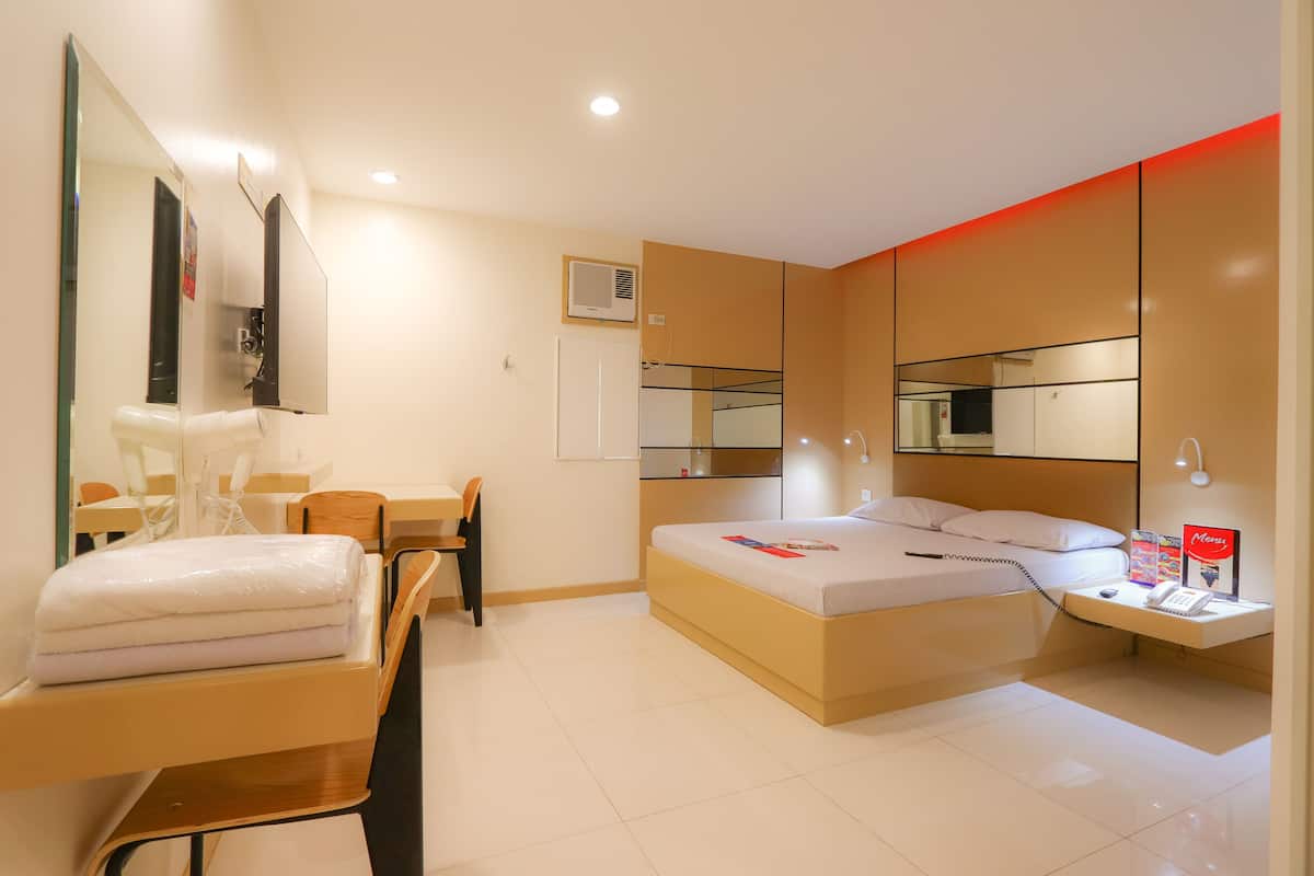 Ein modernes Hotelzimmer mit Bett, Nachttisch, Stuhl, Schreibtisch und einem großen Spiegel.
