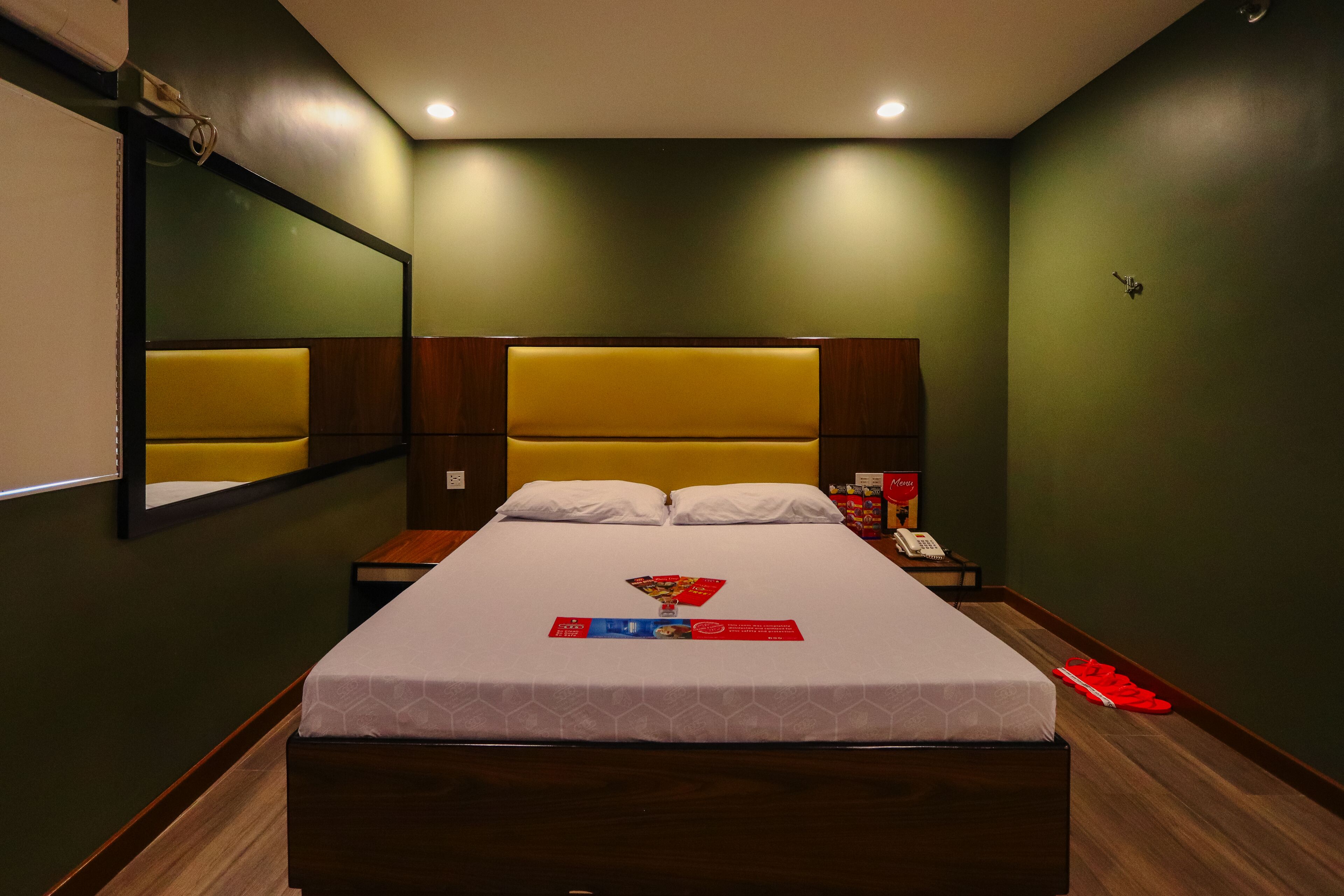 A hotel room with a large bed, a bedside table, a mirror, and a nightstand.
