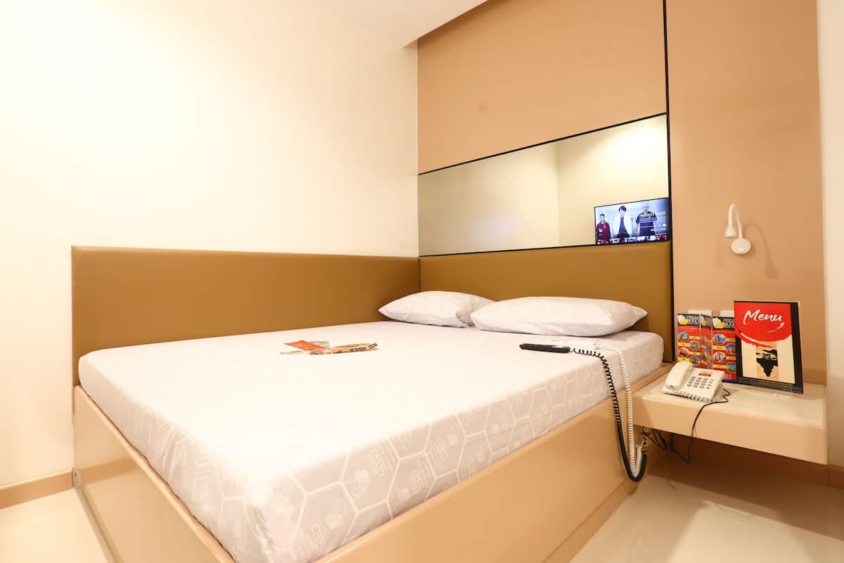 Ein Hotelzimmer mit Bett, Nachttischtelefon, einer kleinen Ablage mit Speisekarten und einem an der Wand montierten Fernseher.