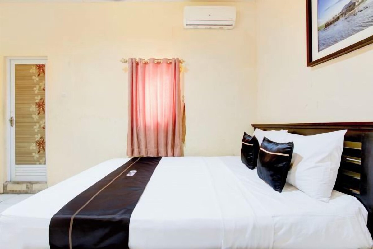 Een hotelkamer met een bed, gordijn, airconditioning en een lijst met een afbeelding aan de muur.