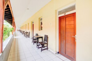 A corridor with wooden tables and chairs, a tiled floor, and a wooden door with a number. - Collection O Stasiun Pekalongan Near Stasiun Kereta Api Formerly Hotel Indah (Pekalongan)