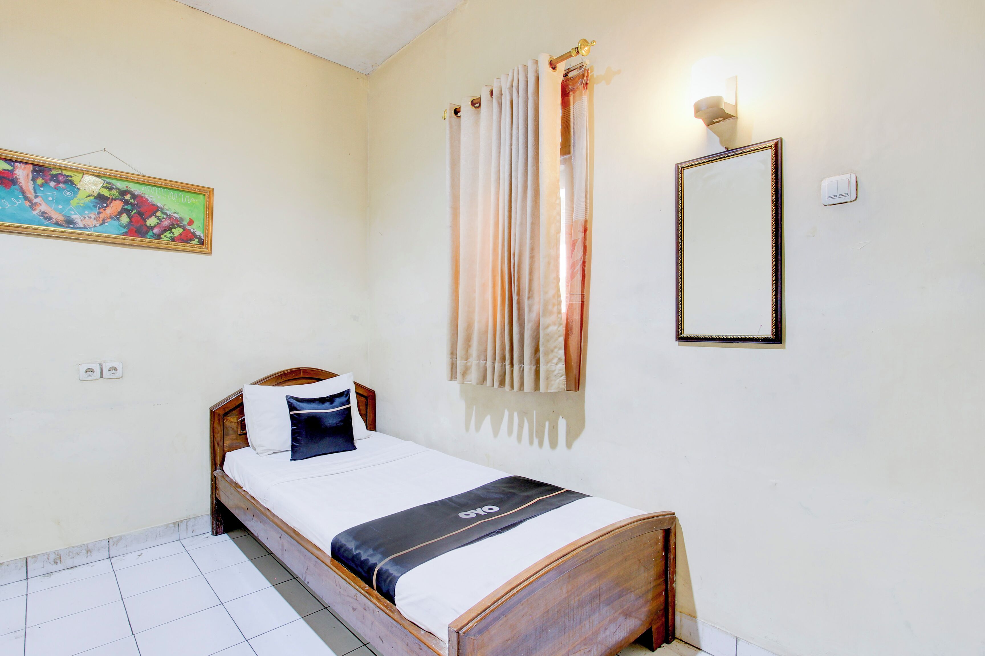 A single bed with a wooden frame, white bedding, and a black accent. A painting is on the wall, and a mirror is above the bed.