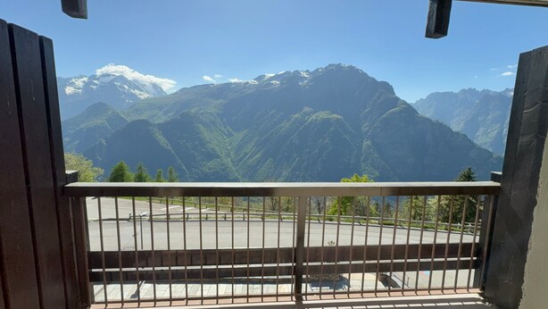 A balcony with a view of snow-capped mountains and a paved area below.