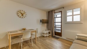 A room with a wooden desk, a chair, a television, a window with curtains, and a sofa.