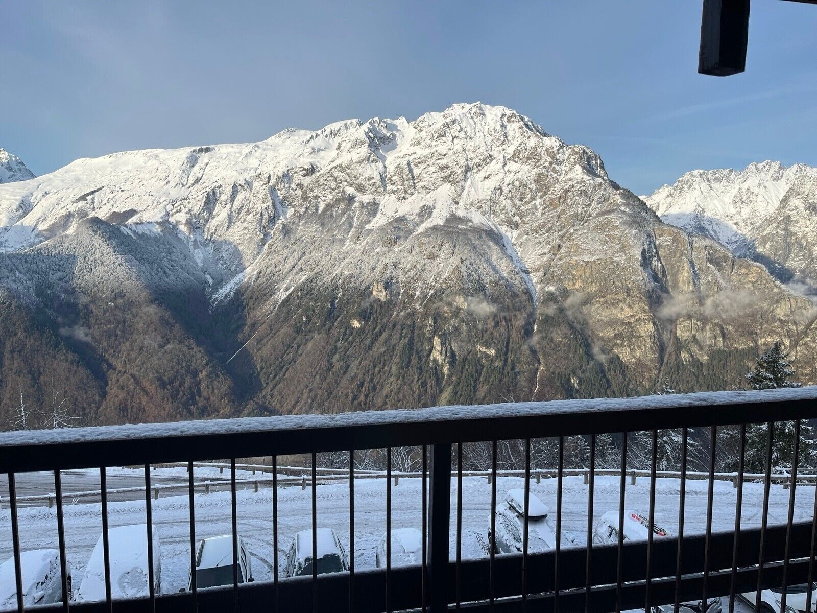 A mountain landscape with snow-covered peaks and a view of a parking area with cars.