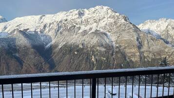 A mountain landscape with snow-covered peaks and a view of a parking area with cars.
